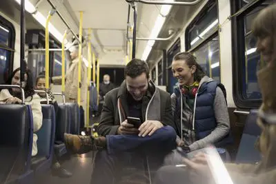 Casal jovem sorridente trocando mensagens de texto com o smartphone no ônibus