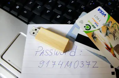 Cartões de crédito e um pen drive sentado em um laptop com uma senha escrita no papel.