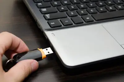 Mão inserindo uma chave USB na porta USB de um laptop