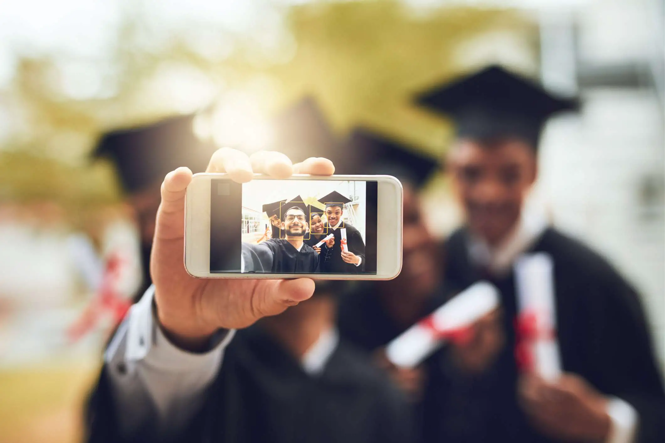 Um grupo de graduados tirando uma selfie para smartphone com reconhecimento facial ativado. 