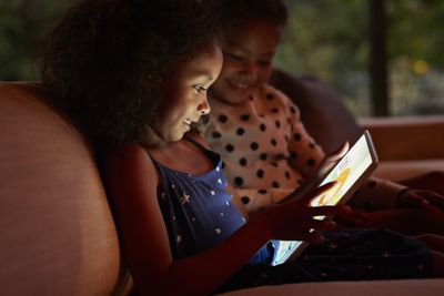 Duas meninas brincando no tablet digital, à noite.