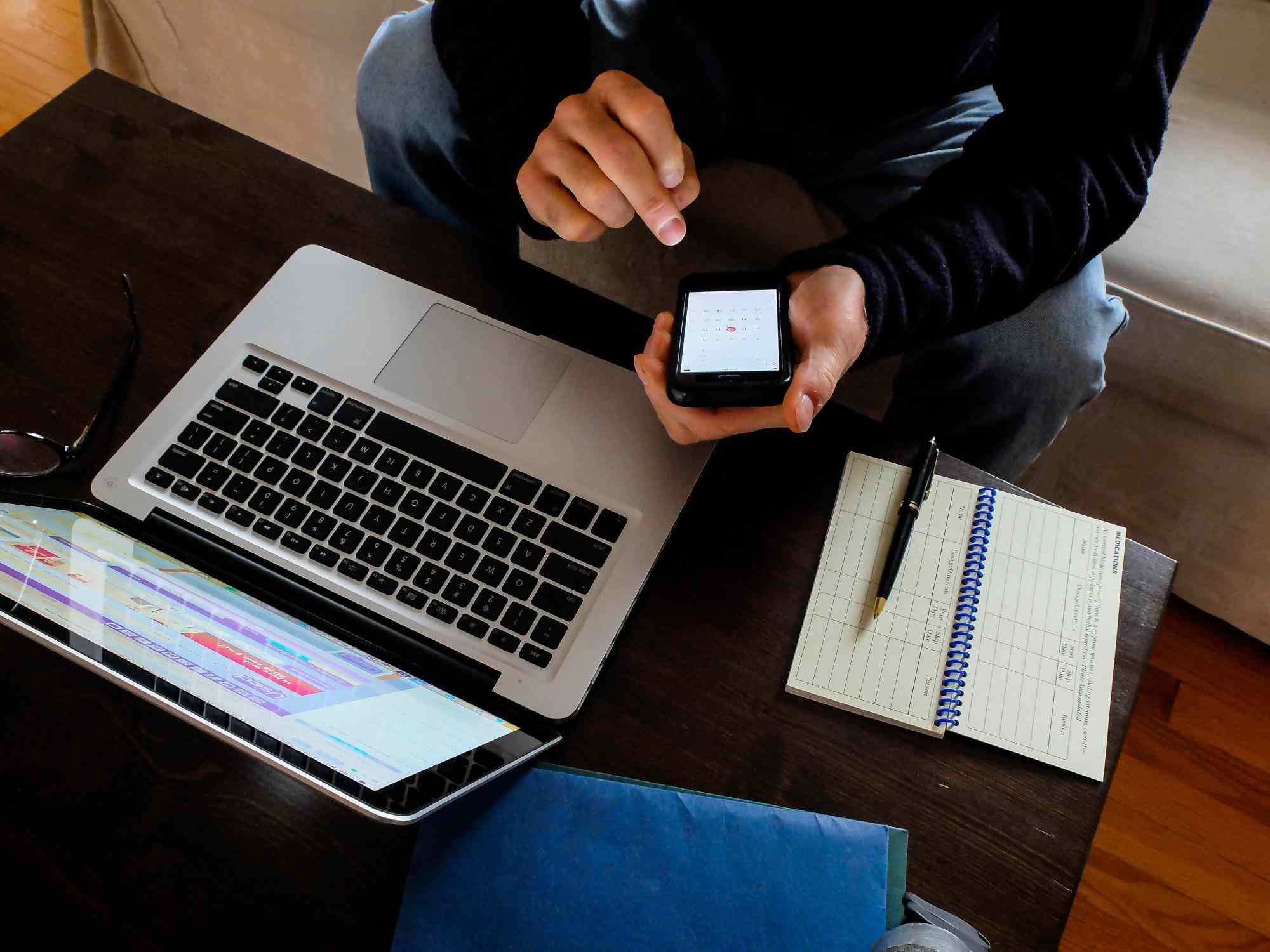 Um homem trabalhando em sua mesa de centro com um laptop, telefone e planejador.