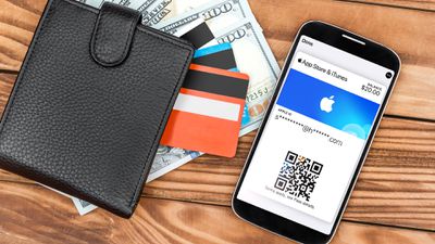 Um iPhone com o aplicativo iOS Wallet aberto, mostrando a App Store e o iTunes Pass ao lado de uma carteira cheia de dinheiro e cartões de crédito.