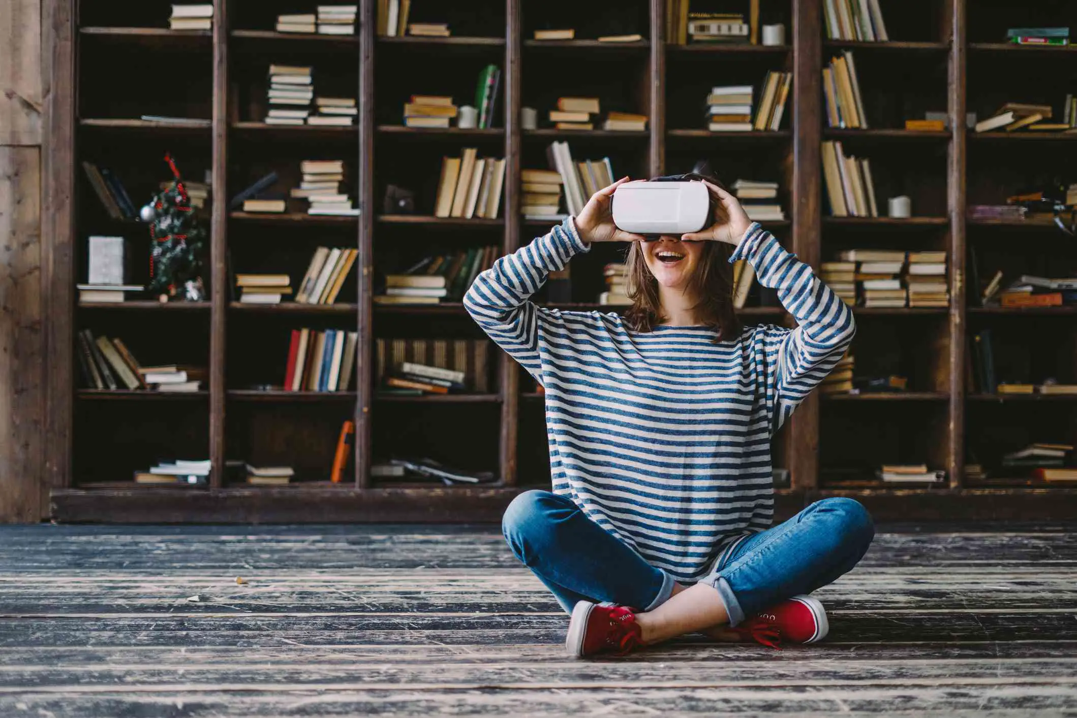 Alguém sentado no chão usando a tecnologia VR em frente às estantes de livros.