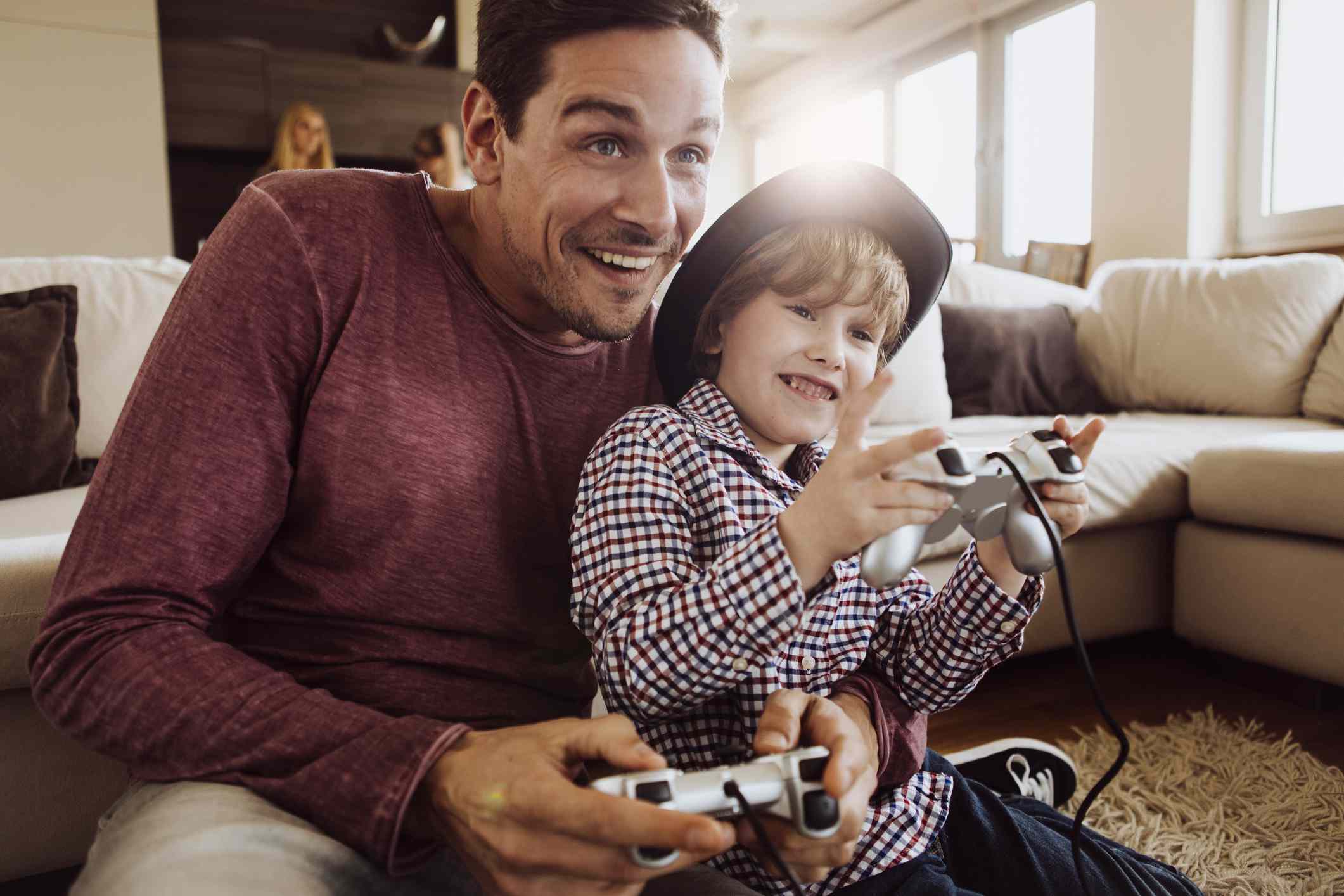 Pai e filho jogando PlayStation juntos, sentados no chão da sala. 