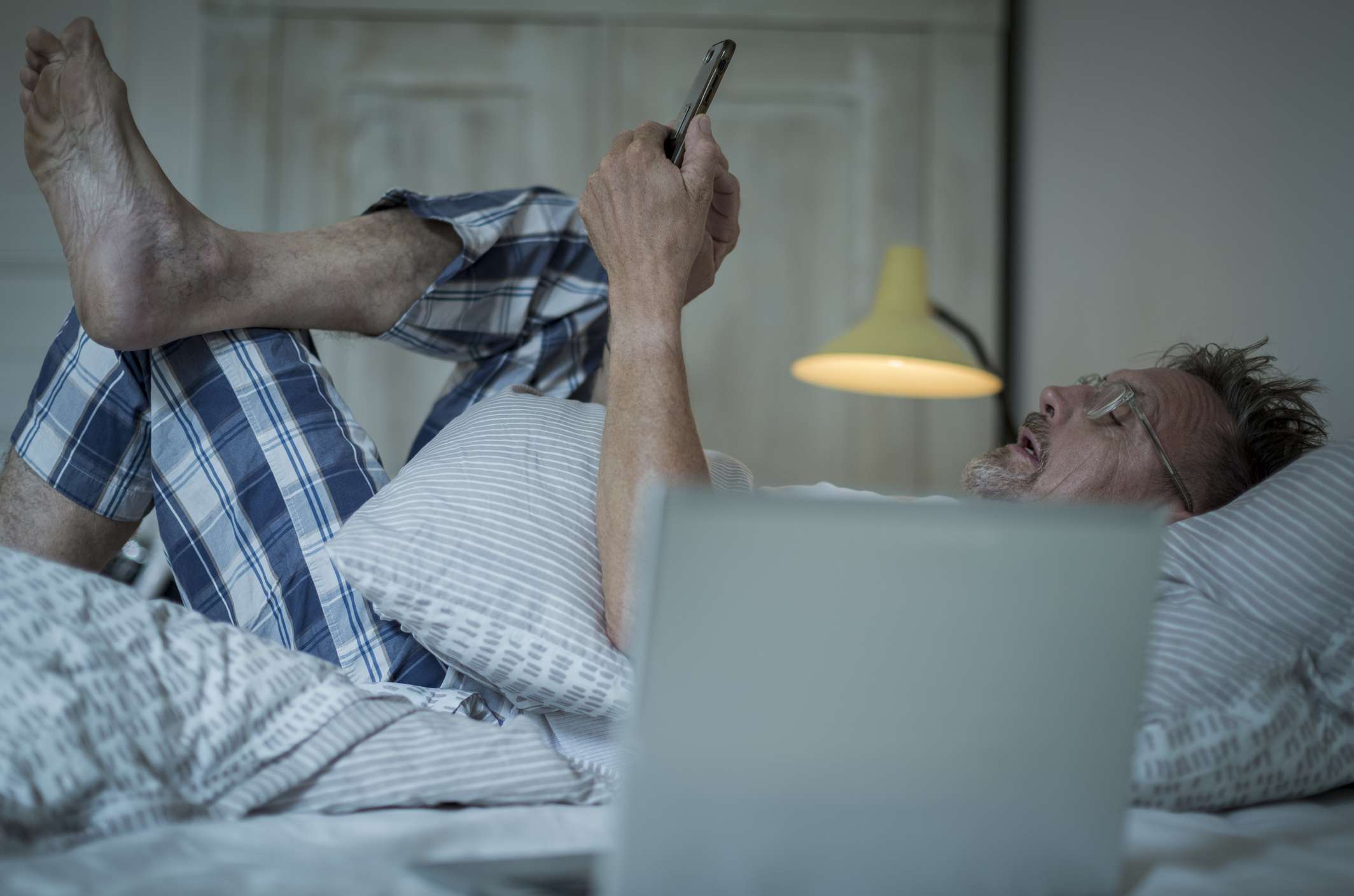 Homem com barba grisalha e sem dormir na cama à noite usando laptop e smartphone