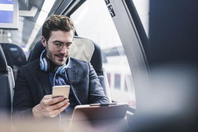 Empresário no trem com celular, fone de ouvido e tablet