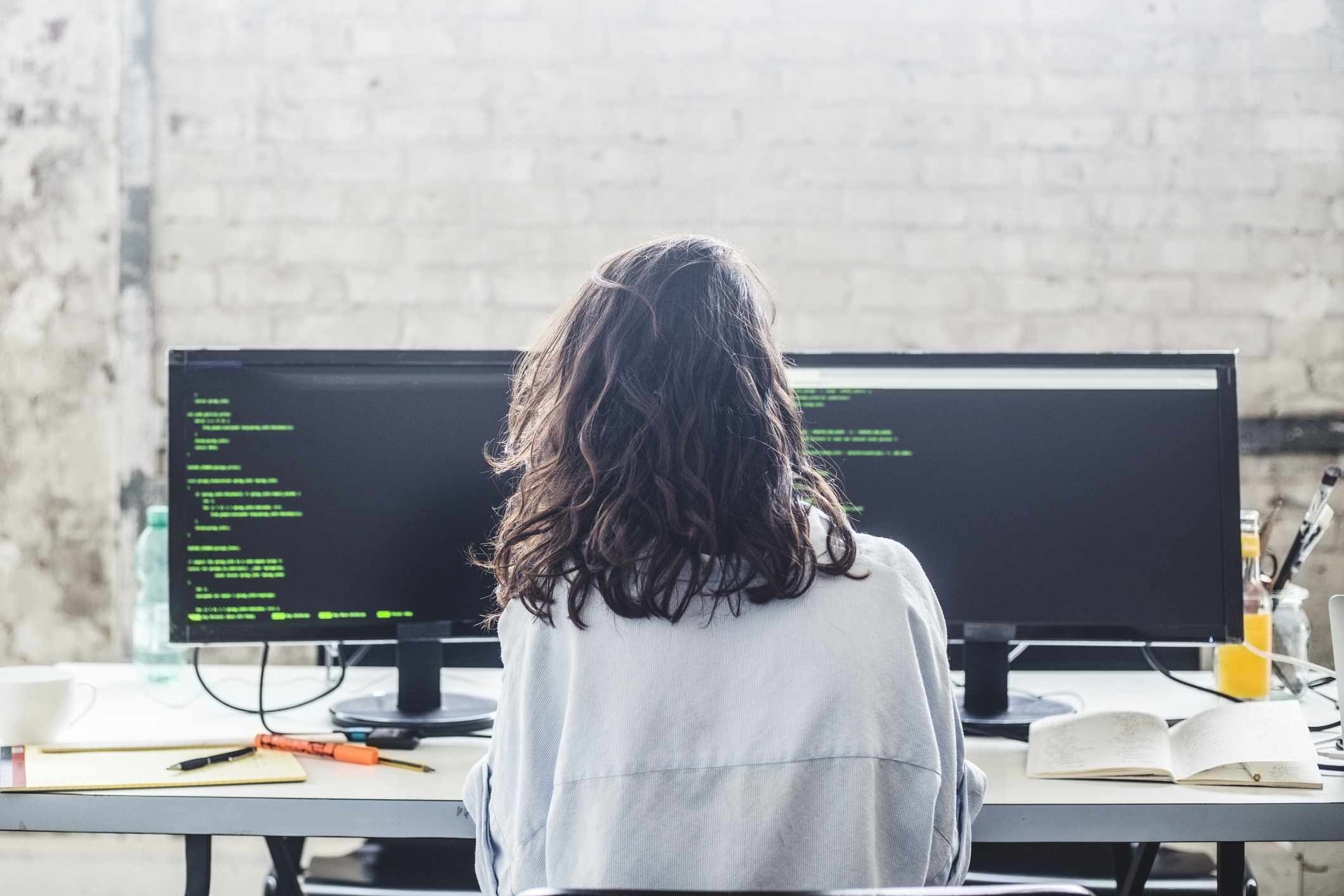 Vista traseira do hacker de computador feminino codificando na mesa do escritório criativo