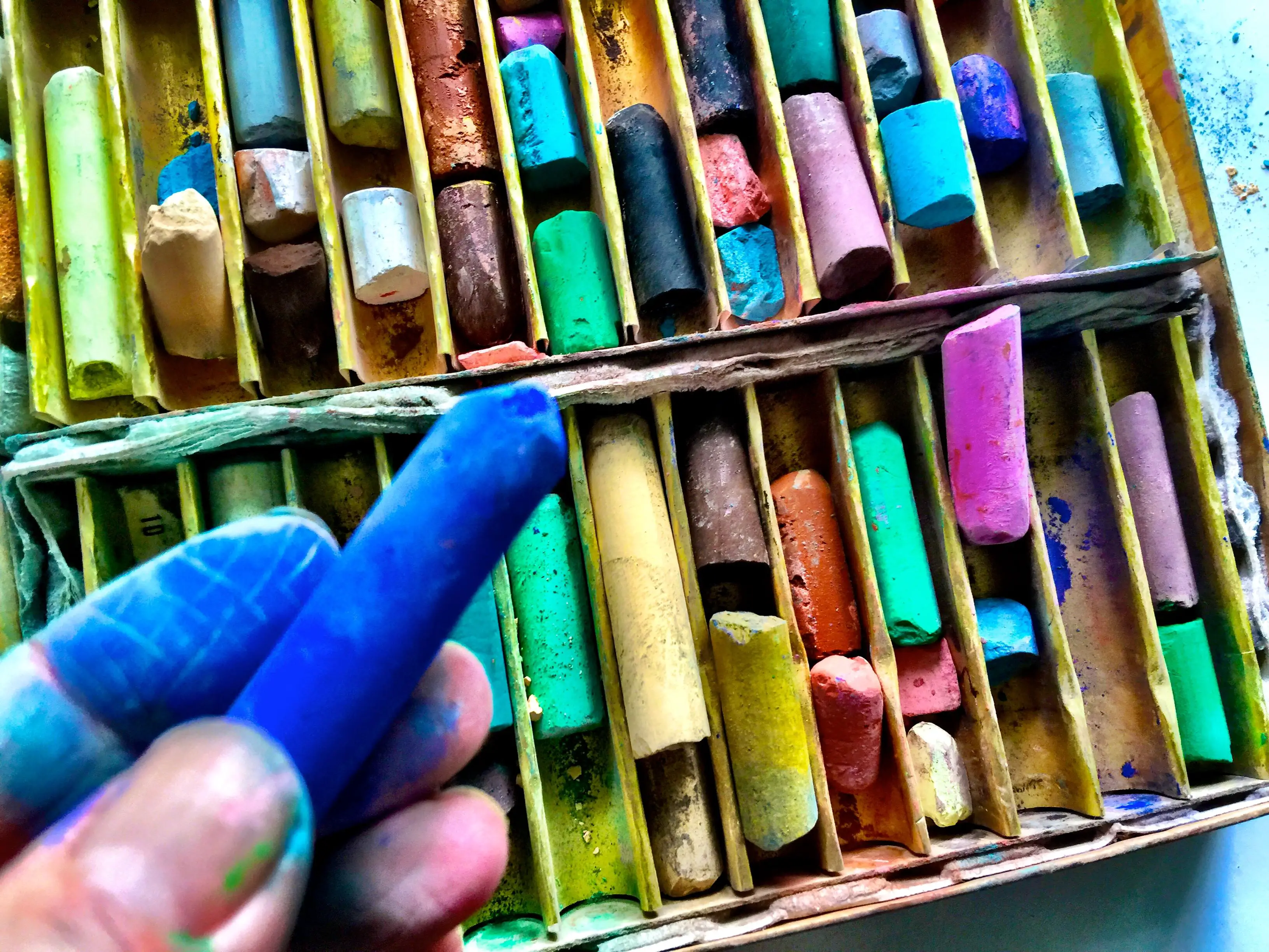 Mão recortada segurando lápis pastel azul sobre a caixa