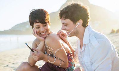 Homem e mulher compartilhando música na praia com cabos AUX e fones de ouvido