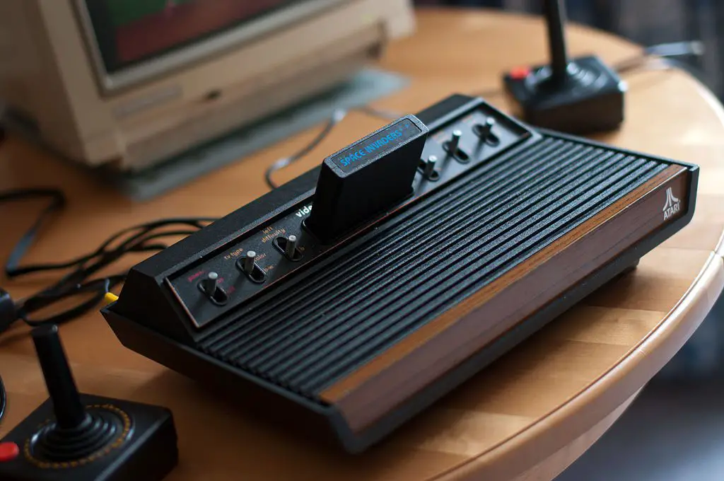 Console Atari 2600 VCS, visualização completa, com joysticks e monitor Commodore 1084S parcialmente visíveis.  1978 modelo de seis interruptores.  O jogo Space Invaders é inserido.