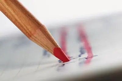 Um lápis vermelho marcando a caligrafia no papel.