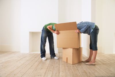 Casal jovem desempacotando caixa em nova casa com rostos escondidos