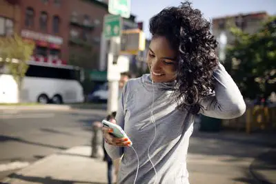 Mulher olhando para o iPhone e usando fones de ouvido em uma rua da cidade