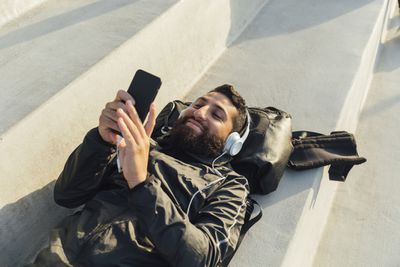 Homem deitado de costas, ouvindo fones de ouvido e usando um iPhone