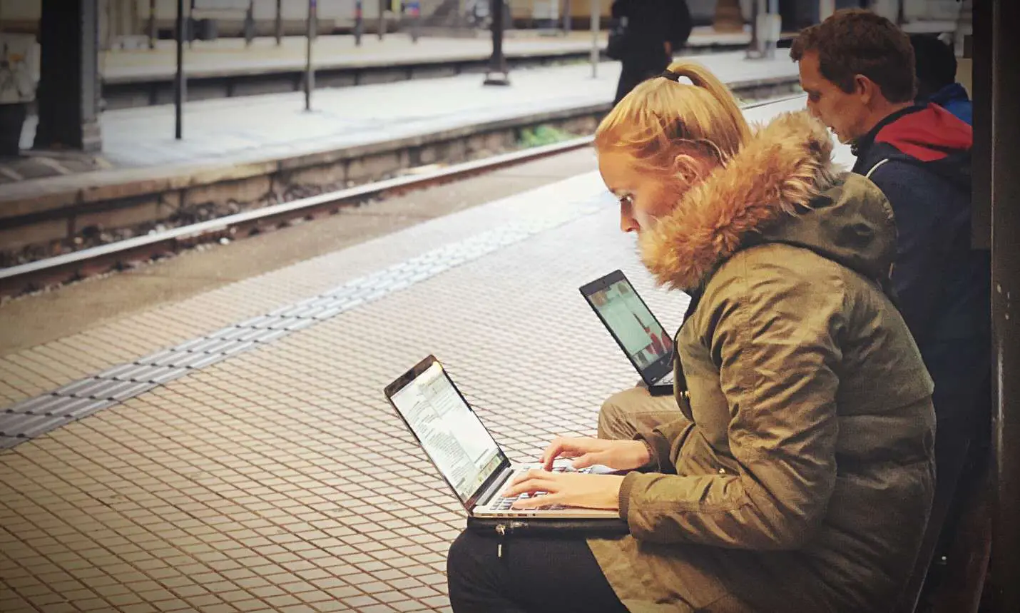 Pessoas esperando em uma estação de trem usando computadores laptop.