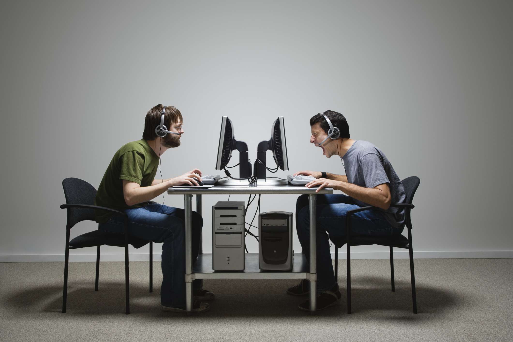 Um perfil de dois homens usando computadores sentados frente a frente em uma mesa