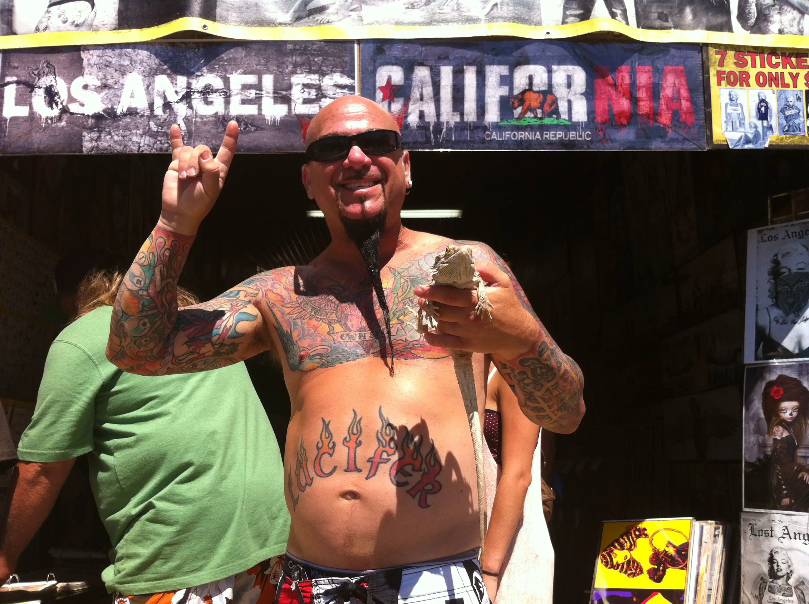 Homem tatuado em frente ao banner de Los Angeles segurando um lagarto