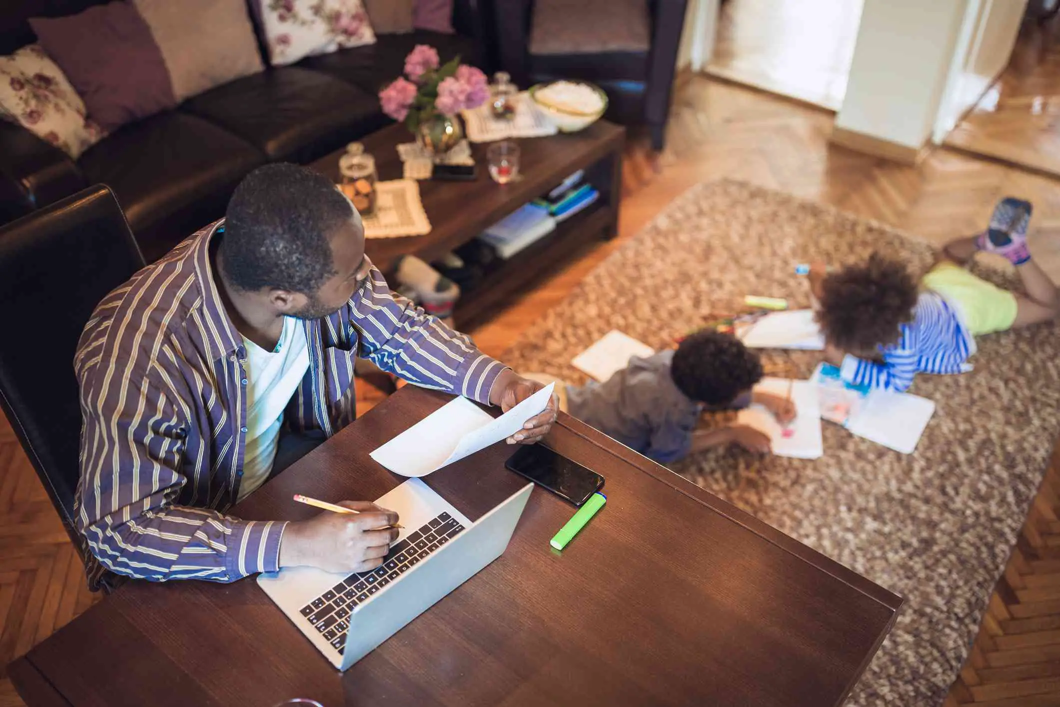 Pai trabalhando em casa enquanto seus dois filhos brincam na sala de estar