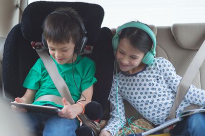 Criança jogando no tablet no carro enquanto a irmã assiste
