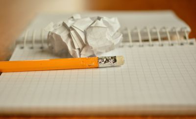 Um caderno com um lápis e papel amassado sobre ele.