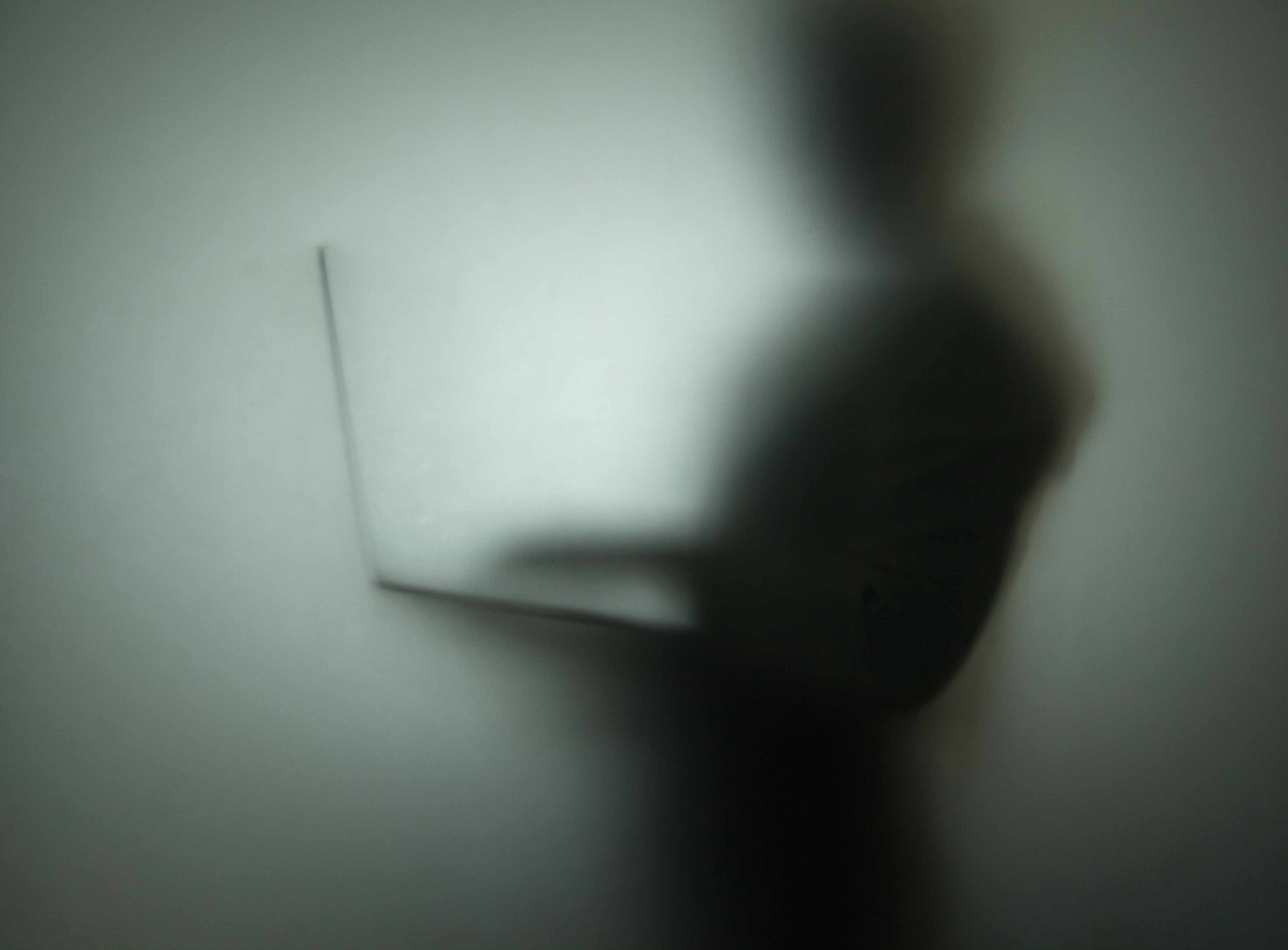 Foto de uma silhueta de uma pessoa usando um laptop atrás de um vidro