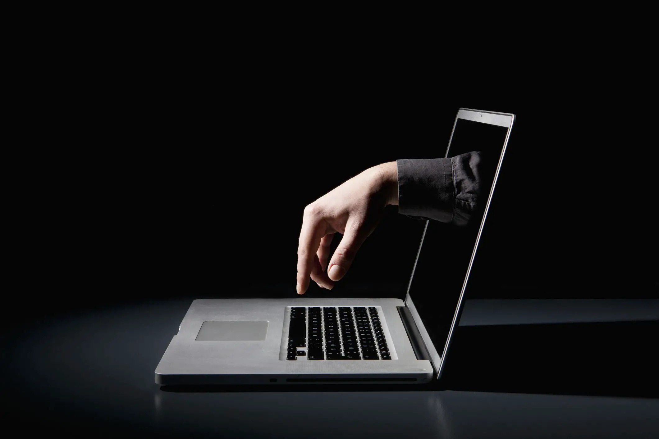 Uma mão alcançando um laptop para digitar no teclado