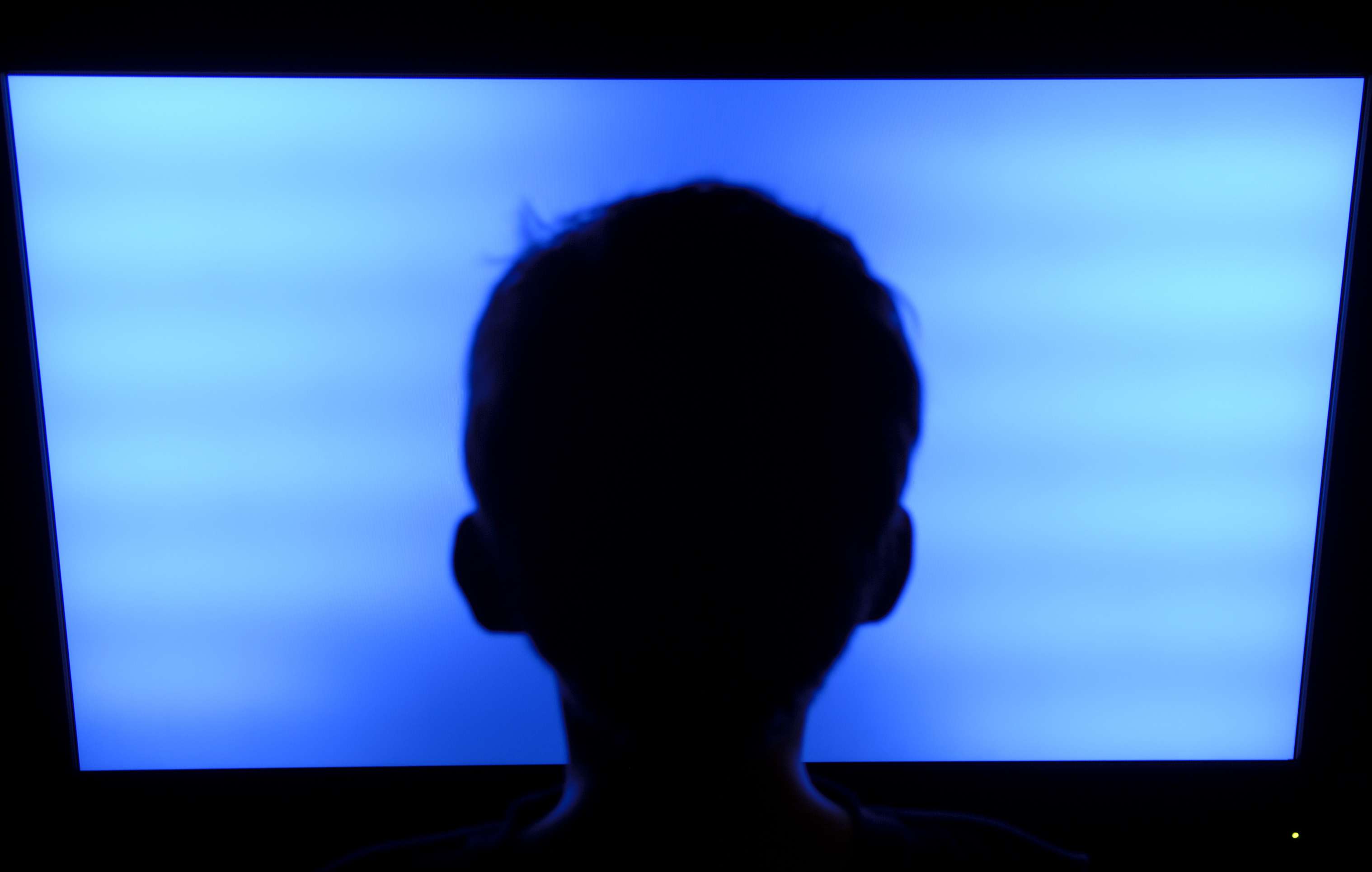 Silhueta da cabeça de uma criança em frente a uma TV de tela plana