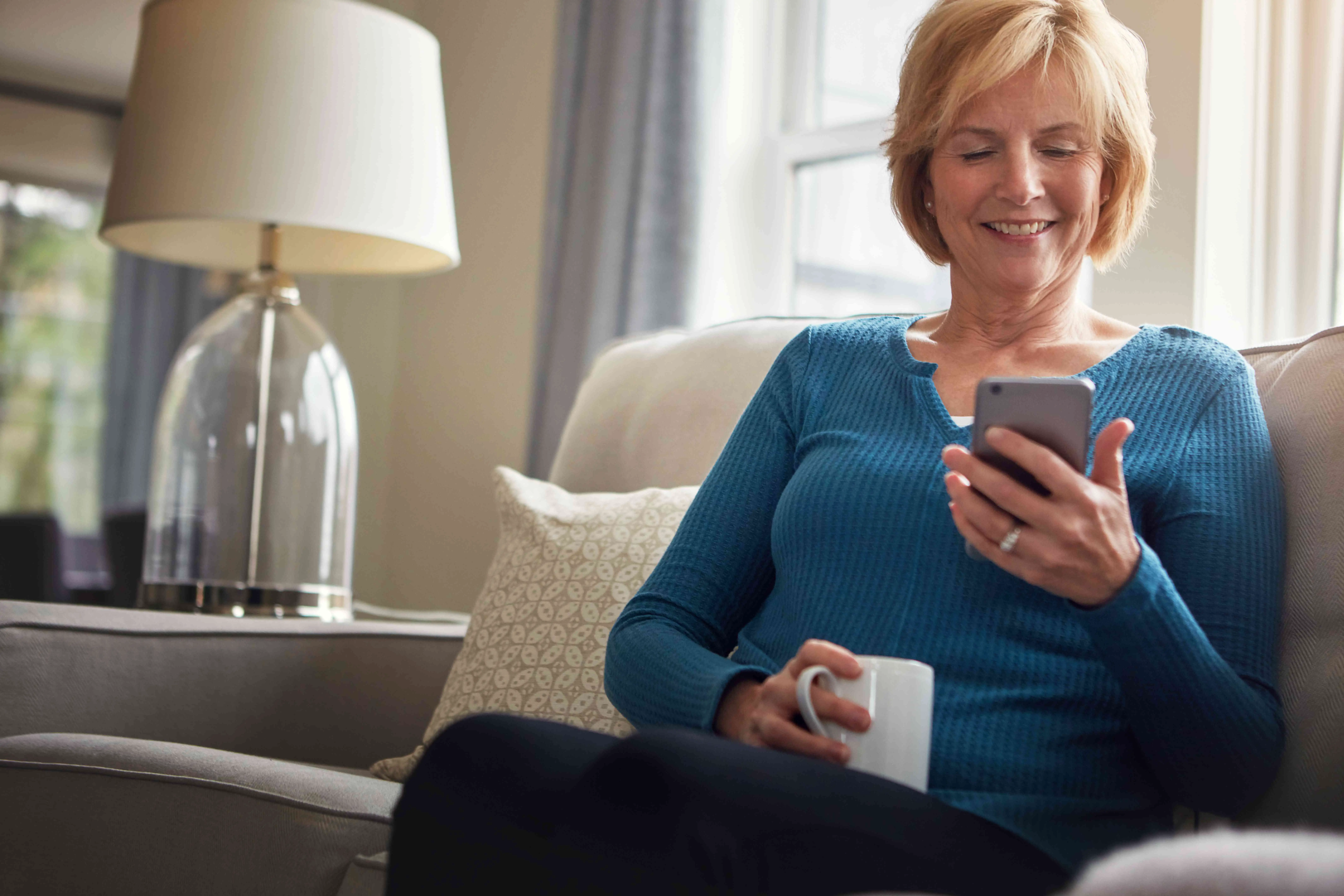 Uma mulher está sentada em um sofá e olhando para um telefone celular.