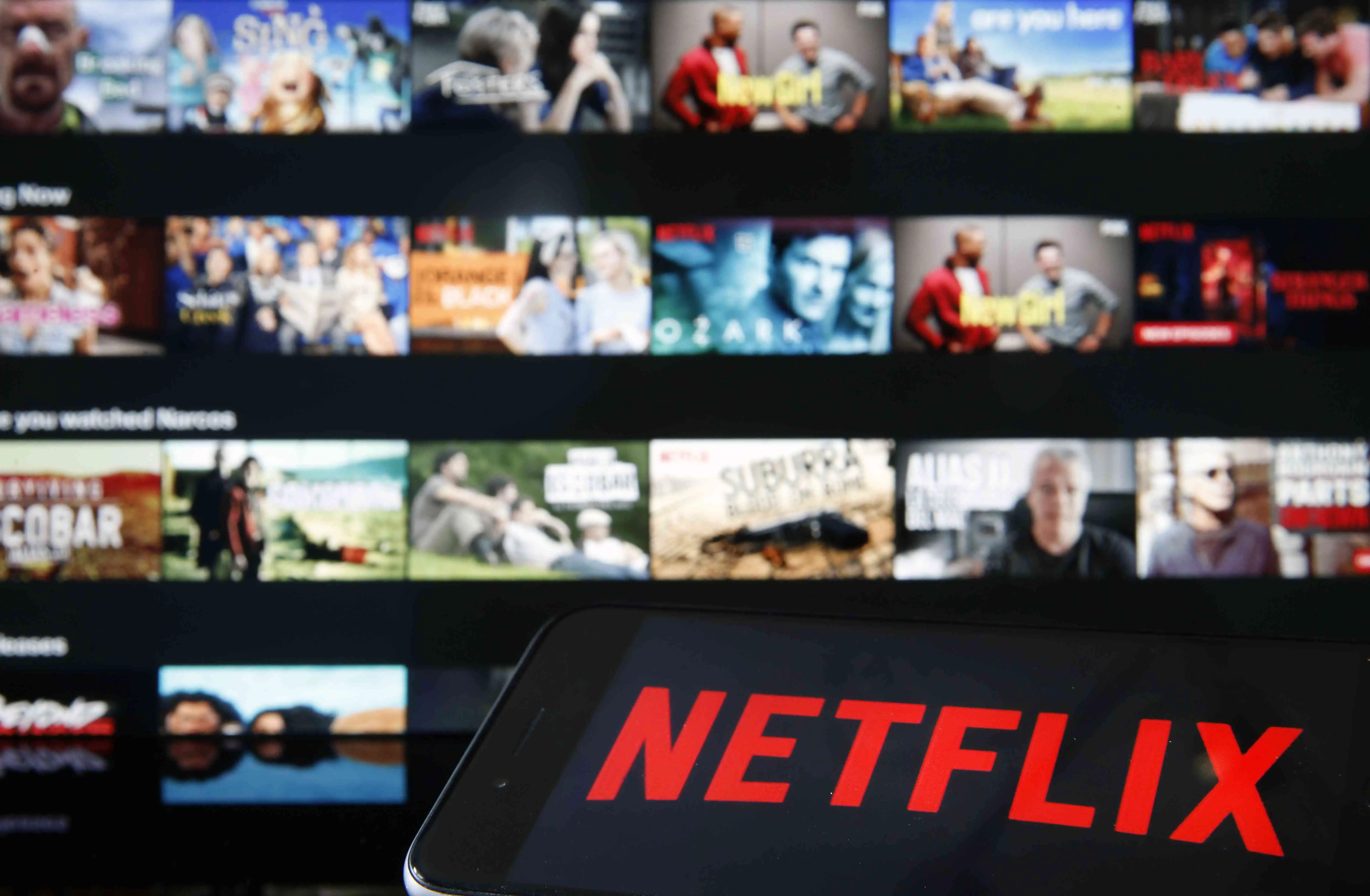 Logotipo da Netflix exibido em um iPhone na frente de uma televisão exibindo Netflix