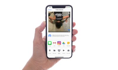 Uma mão segurando um iPhone com um vídeo selecionado e o menu de compartilhamento.