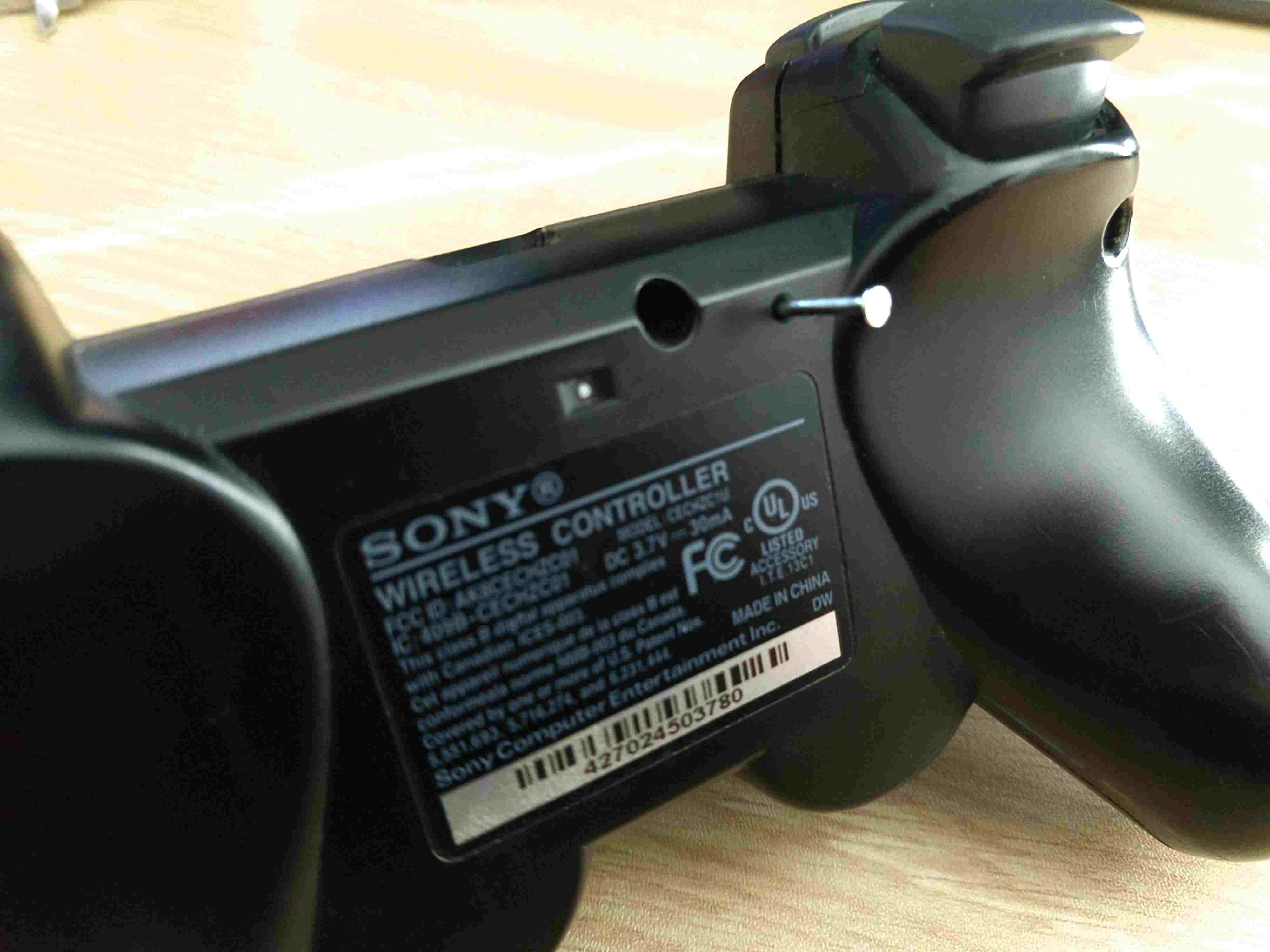 Uma ferramenta inserida no orifício de acesso do botão de reset em um controlador PS3