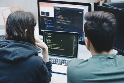 Duas pessoas olhando para o código na tela do notebook.