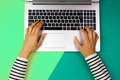 Mãos cortadas de mulher usando laptop sobre fundo colorido