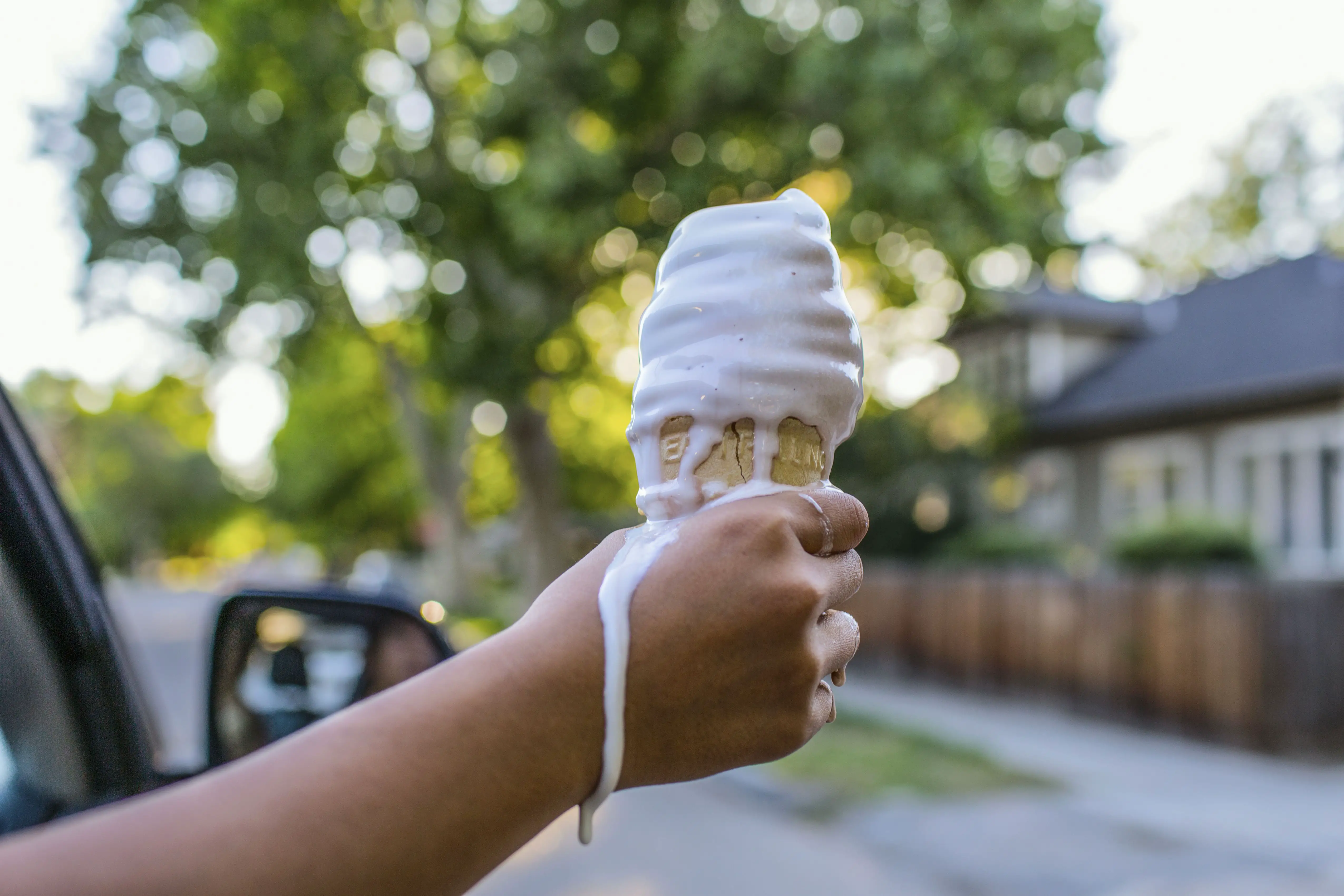 Close da mão de uma menina segurando casquinha de sorvete derretendo
