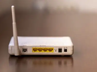 Parte traseira de um roteador de modem mostrando entrada ADSL, portas Ethernet e antena WiFi