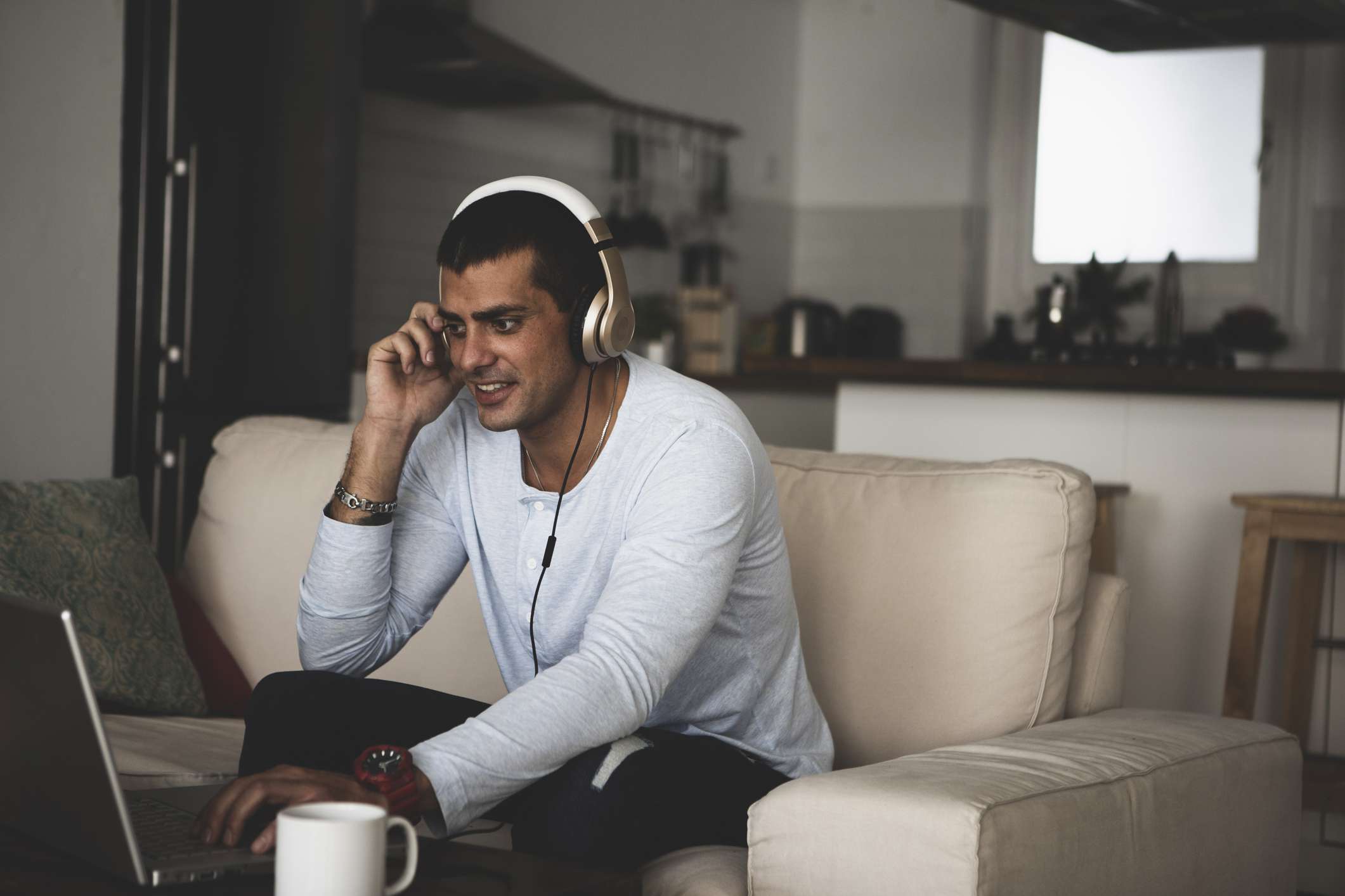 Um homem sentado em um sofá com fones de ouvido e olhando para um laptop