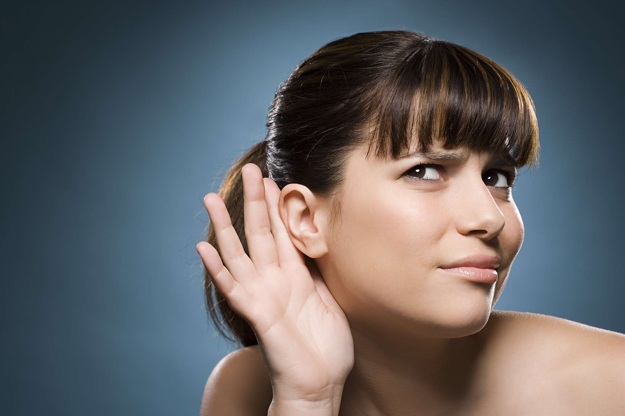 Foto de uma mulher com a mão no ouvido para ouvir melhor