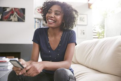 Mulher afro-americana sorridente com o celular no sofá da sala