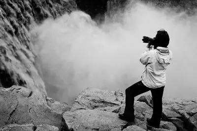 Um fotógrafo tirando uma foto de uma cachoeira na Islândia.