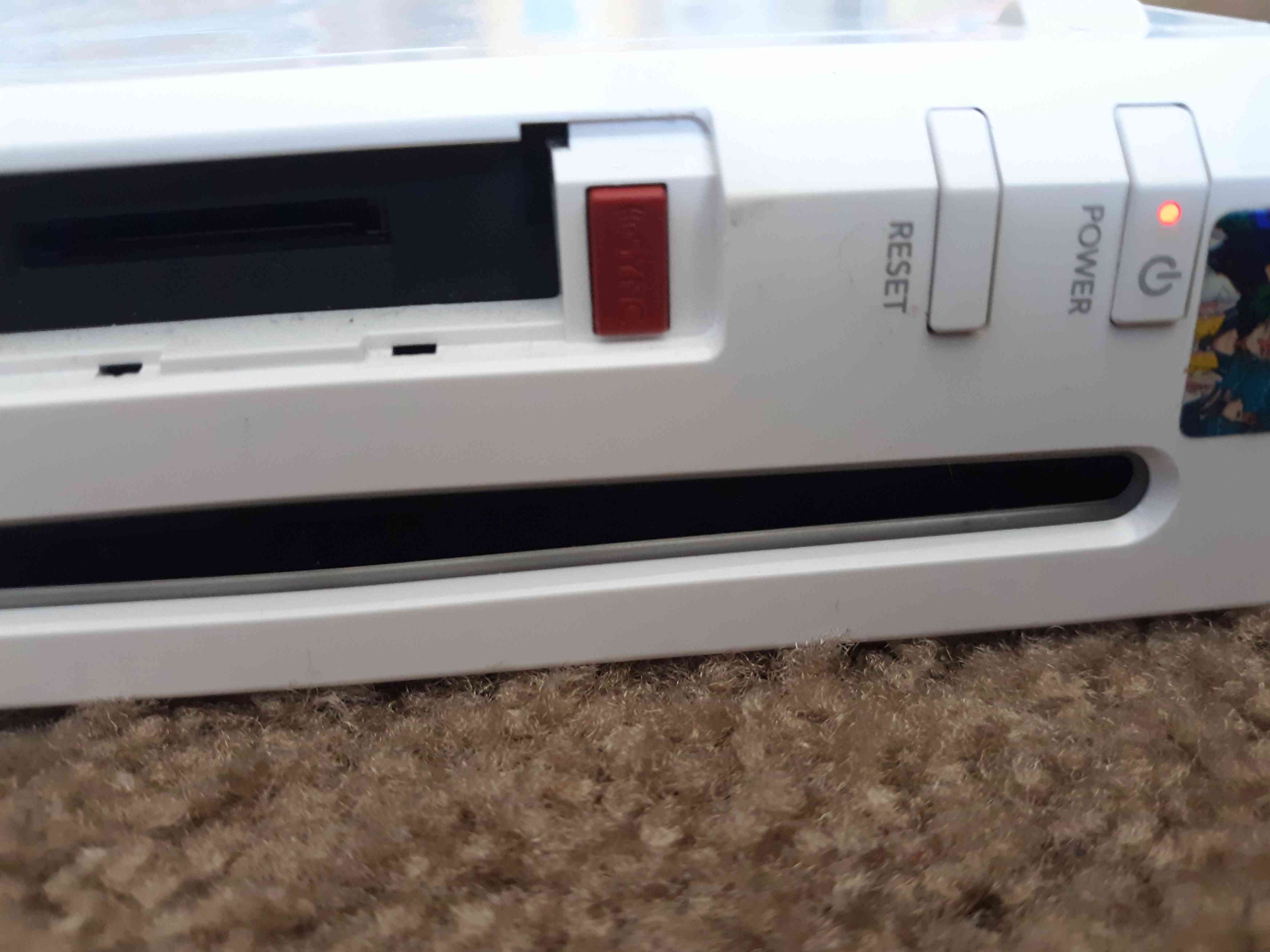O botão de sincronização vermelho está sob a tampa do slot do cartão de memória na frente do console Wii.