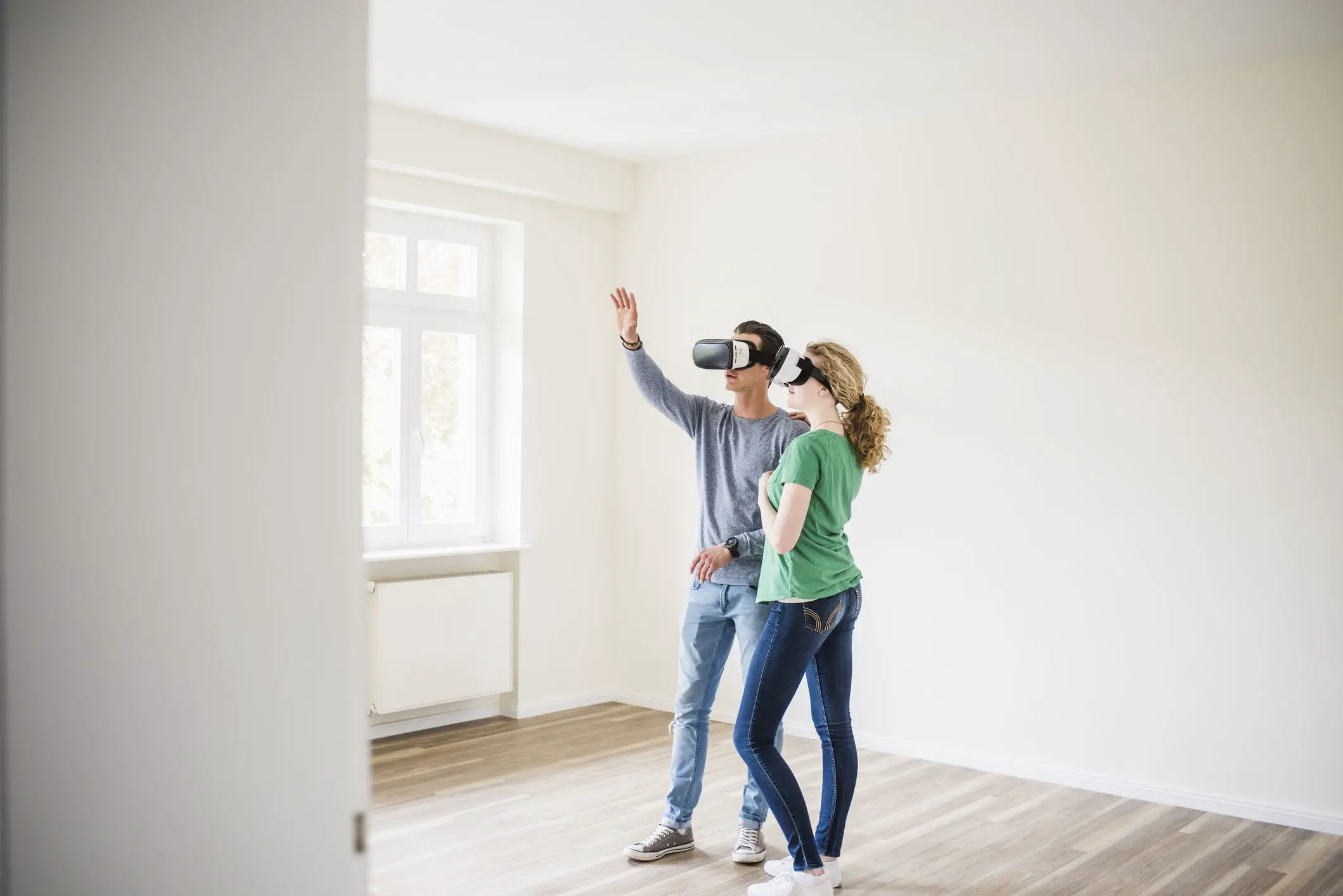 Um casal de pé em um apartamento vazio usando óculos de realidade virtual. 