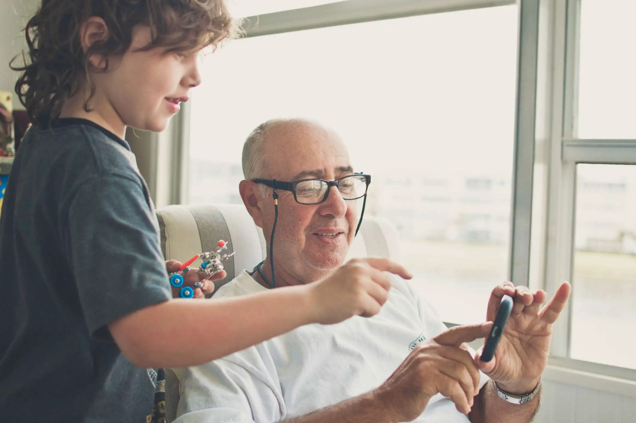 Um avô e um neto interagindo com um smartphone enquanto a criança segura um pequeno robô.