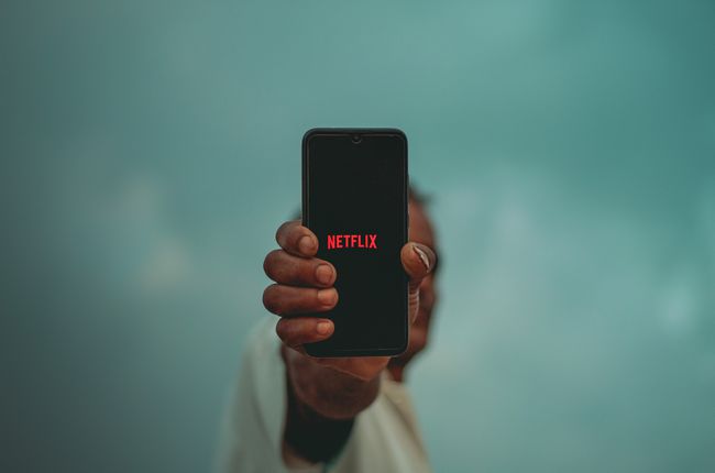 Uma pessoa segurando um iPhone preto no comprimento do braço com o logotipo da Netflix na tela. 
