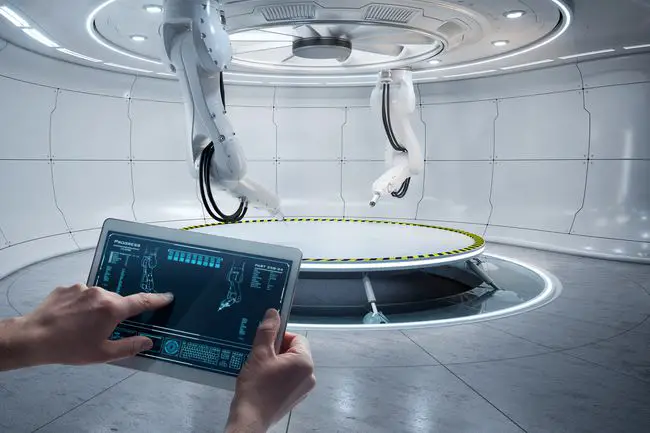 Dois braços robóticos em um laboratório sendo controlados por alguém usando um tablet.