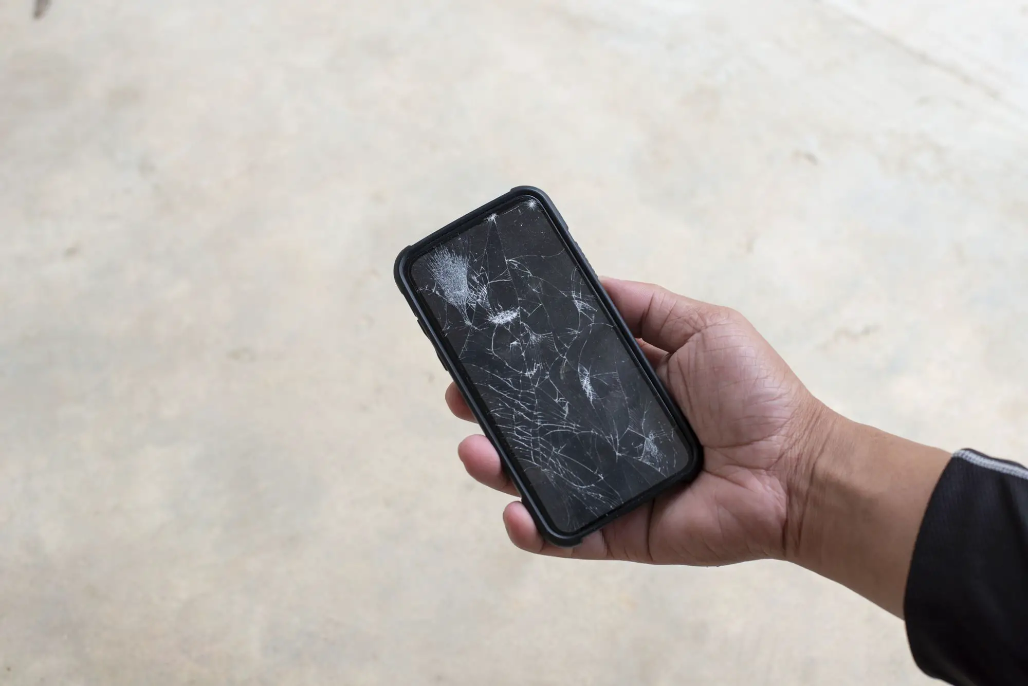 Uma mão segurando um smartphone com uma tela quebrada.
