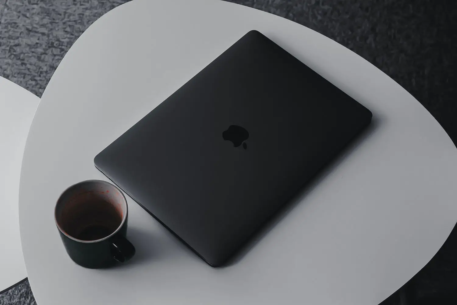 Laptop MacBook preto descansando na mesa de centro com caneca de café