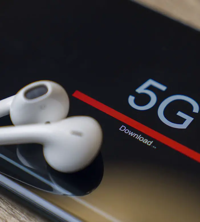 Telefone mostrando um download 5G com fones de ouvido sobre ele.